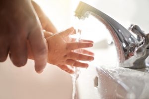 adult-holding-child-hands-at-sink-faucet