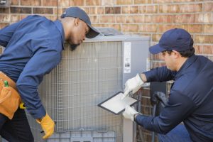 two-techs-in-front-of-ac-outdoor-unit-looking-at-tablet