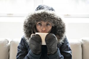 woman-in-parka-huddled-on-couch-drinking-of-of-mug