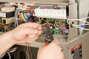 Technician using wire strippers while working on electrical wiring during a heater replacement.